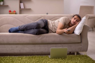 Evdeki kanepede yatan genç adam.