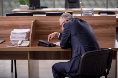 Eski erkek çalışan ofiste oturuyor.