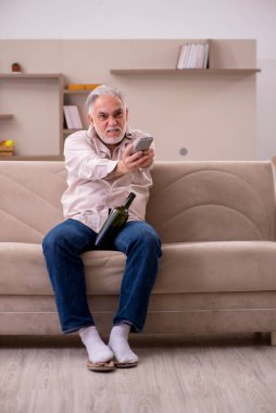 Yaşlı adam evde alkol içiyor.