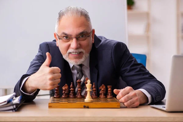 Viejo empleado jugando ajedrez en el lugar de trabajo — Foto de Stock
