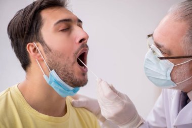 Genç erkek hasta yaşlı doktor otorhinolaryngologis 'i ziyaret ediyor.