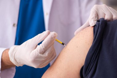 Yaşlı adam covid-19 aşı konseptinde genç doktoru ziyaret ediyor.