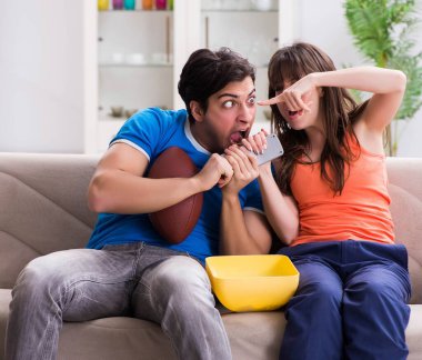 Adam karısıyla Amerikan futbolu seyrediyor.