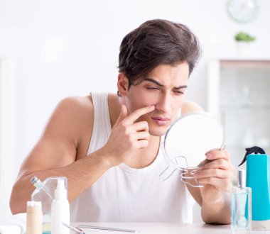 Genç yakışıklı adam aynaya bakıyor.