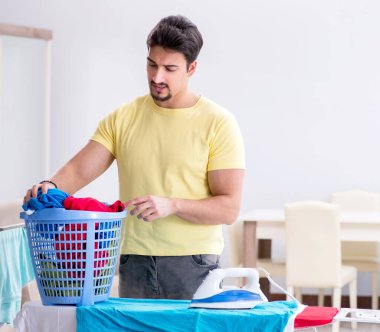 Yakışıklı koca evde kıyafet ütülüyor.