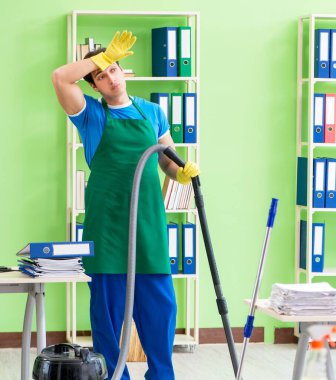 Elektrikli süpürgeyle ofisi temizleyen yakışıklı adam.