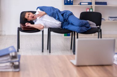 Genç bir erkek çalışan ofiste koltuklarda uyuyor.