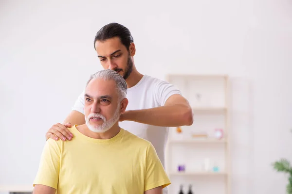 Velho paciente masculino visitando jovem médico chiropractor — Fotografia de Stock