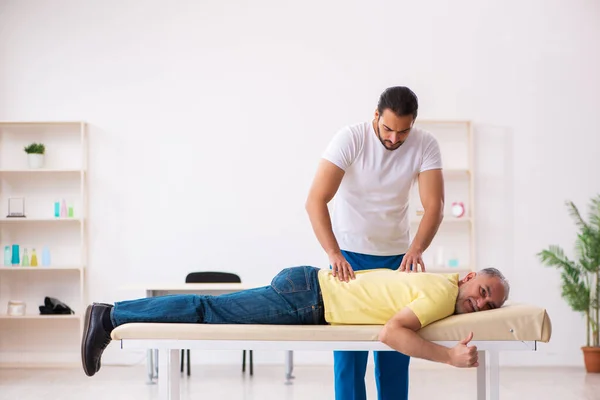 Old male patient visiting young male doctor chiropractor — Stock Photo, Image