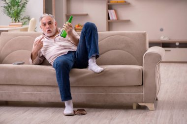 Yaşlı adam evde alkol içiyor.