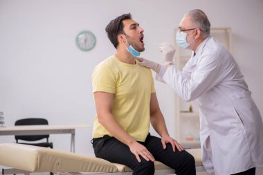 Genç erkek hasta yaşlı doktor otorhinolaryngologis 'i ziyaret ediyor.