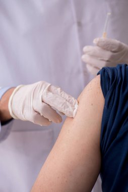 Yaşlı bir erkek hasta aşıyla genç bir doktoru ziyaret ediyor.