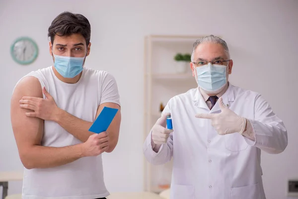 Junge männliche Patientin besucht alten Arzt im Impfpass — Stockfoto