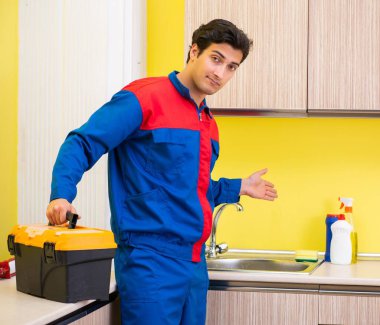 Tesisatçı mutfakta musluğu tamir ediyor.