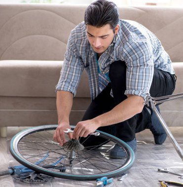 Evde bisiklet tamir eden genç bir adam.