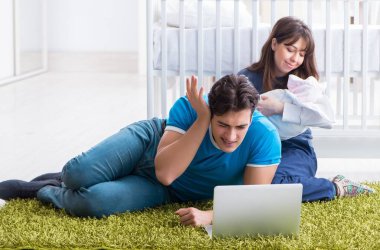 Yeni doğmuş bebekleriyle halıda oturan genç ebeveynler.