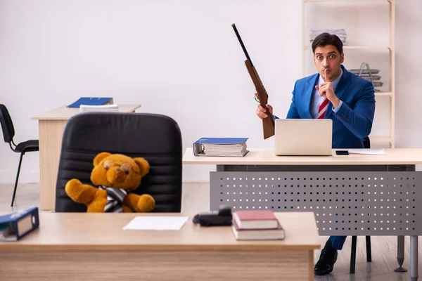 Mladý muž zaměstnanec a jeho hračka medvěd šéf v legrační koncepci — Stock fotografie