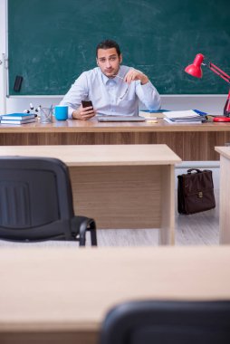 Genç erkek öğretmen yeşil panonun önünde.