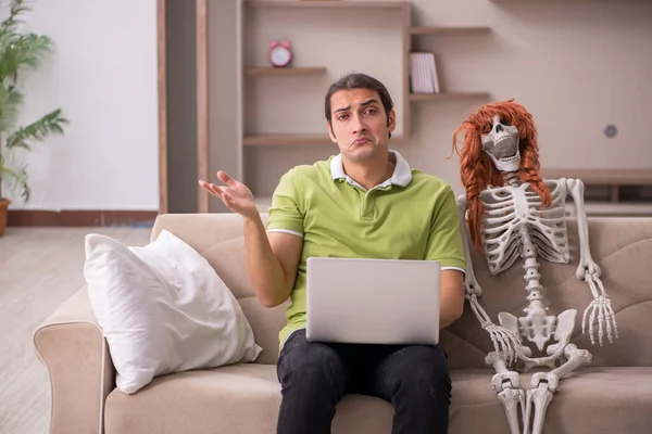 Jovem sentado no sofá com esqueleto feminino — Fotografia de Stock