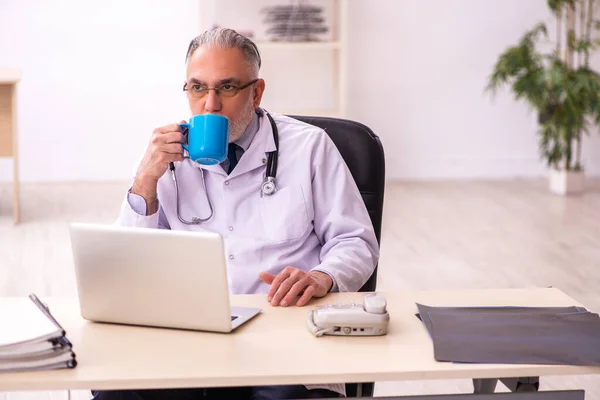 Stárnoucí lékař pije kávu na klinice — Stock fotografie