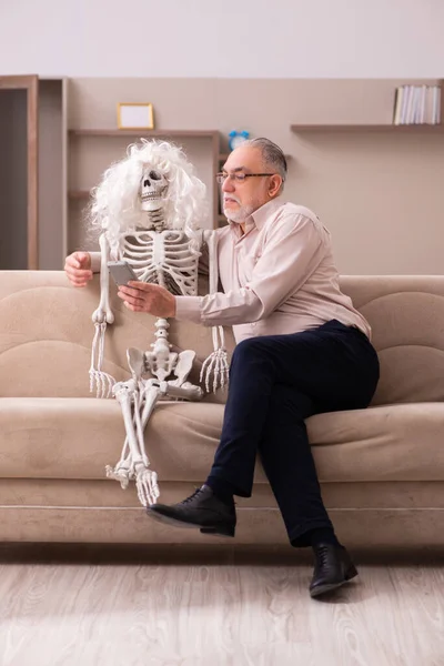 Old man sitting on the sofa with the female skeleton — Stock Photo, Image