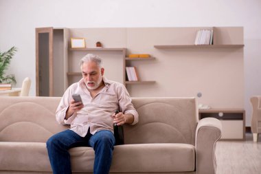 Yaşlı adam evde alkol içiyor.