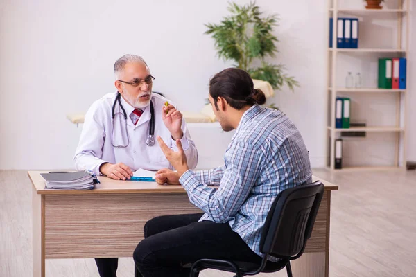 Paciente varón joven que visita al médico varón anciano — Foto de Stock