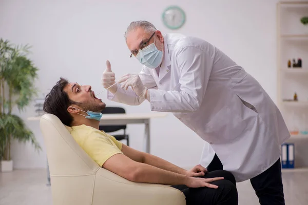 Jonge mannelijke patiënt bezoekt oude mannelijke arts otorhinolaryngologis — Stockfoto