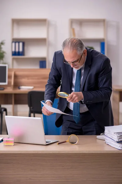 Starý muž zaměstnanec auditor držení loupe na pracovišti — Stock fotografie