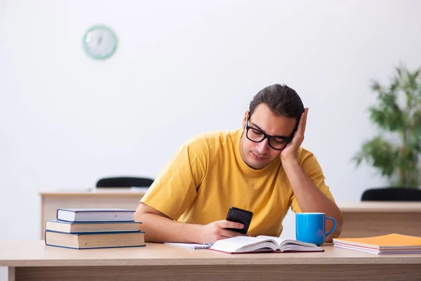 Joven estudiante masculino sosteniendo el teléfono móvil durante la preparación del examen —  Fotos de Stock