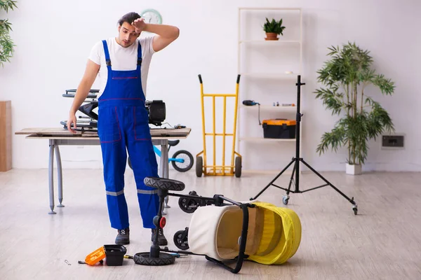 Jonge mannelijke reparateur repareert perambulator binnen — Stockfoto