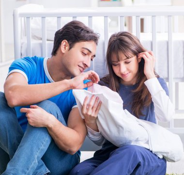 Yeni doğmuş bebekleriyle halıda oturan genç ebeveynler.