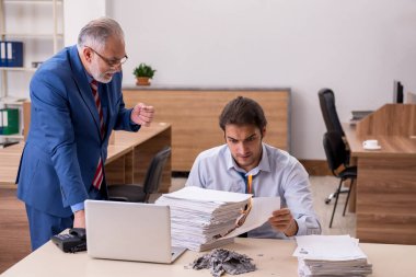 Genç erkek çalışan ve yaşlı patron iş yerinde kağıtları yakıyor.