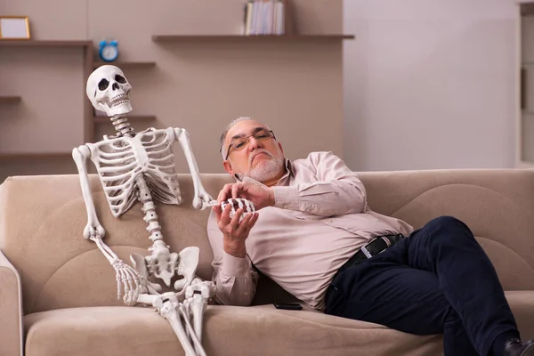 Viejo sentado en el sofá con el esqueleto femenino — Foto de Stock