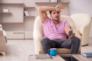 Genç adam salgın sırasında evde televizyon izliyor.