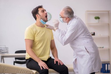 Genç erkek hasta yaşlı doktor otorhinolaryngologis 'i ziyaret ediyor.