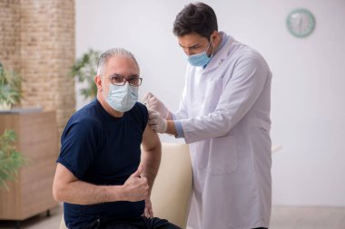 Yaşlı bir erkek hasta aşıyla genç bir doktoru ziyaret ediyor.