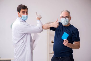 Yaşlı bir erkek hasta aşıyla genç bir doktoru ziyaret ediyor.