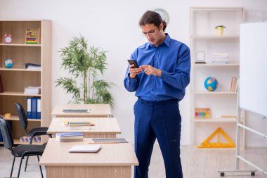 Genç erkek öğretmen ders sırasında elinde akıllı telefon tutuyor.