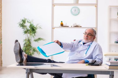 Yaşlı erkek doktor klinikte not alıyor.