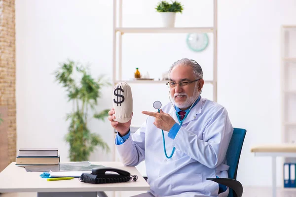 Oude mannelijke dokter met geldzak in het ziekenhuis — Stockfoto