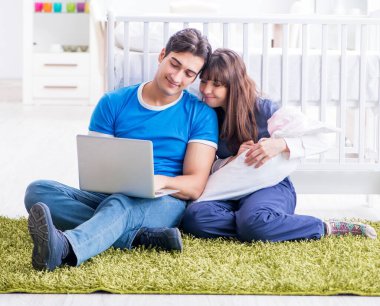 Yeni doğmuş bebekleriyle halıda oturan genç ebeveynler.