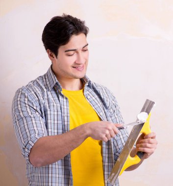 Evdeki duvara alçı yapıştıran genç adam.