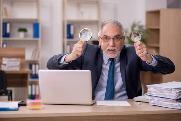 Oude mannelijke werknemer auditor die loupe op de werkplek houdt — Stockfoto