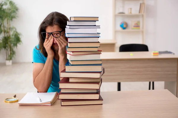 Jonge mannelijke student en veel boeken in de klas — Stockfoto