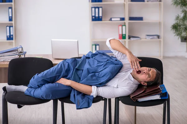 Junge männliche Angestellte schläft im Büro auf Stühlen — Stockfoto
