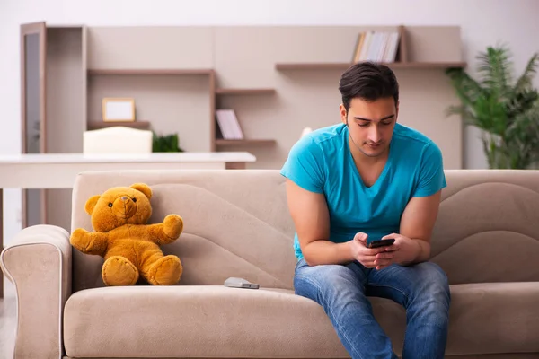 Jovem sentado com urso brinquedo em casa — Fotografia de Stock