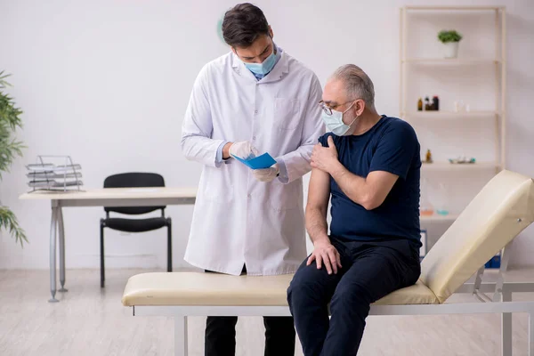 Yaşlı bir erkek hasta aşıyla genç bir doktoru ziyaret ediyor. — Stok fotoğraf