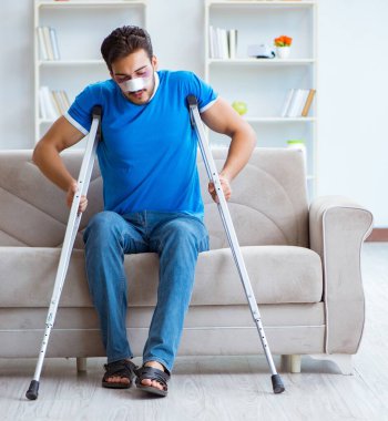 Koltuk değnekli yaralı bir adam evde iyileşiyor.