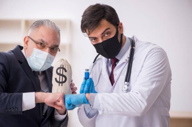Yaşlı işadamı aşı danışmanıyla genç erkek doktoru ziyaret ediyor.
